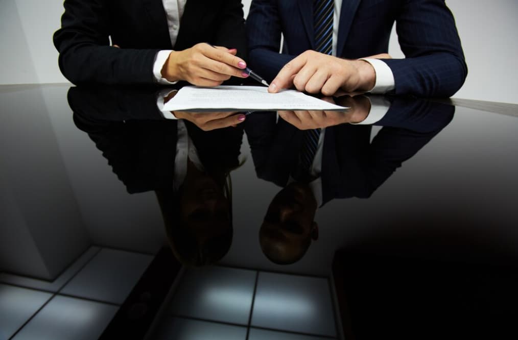Two people signing a contract with a reflective table surface