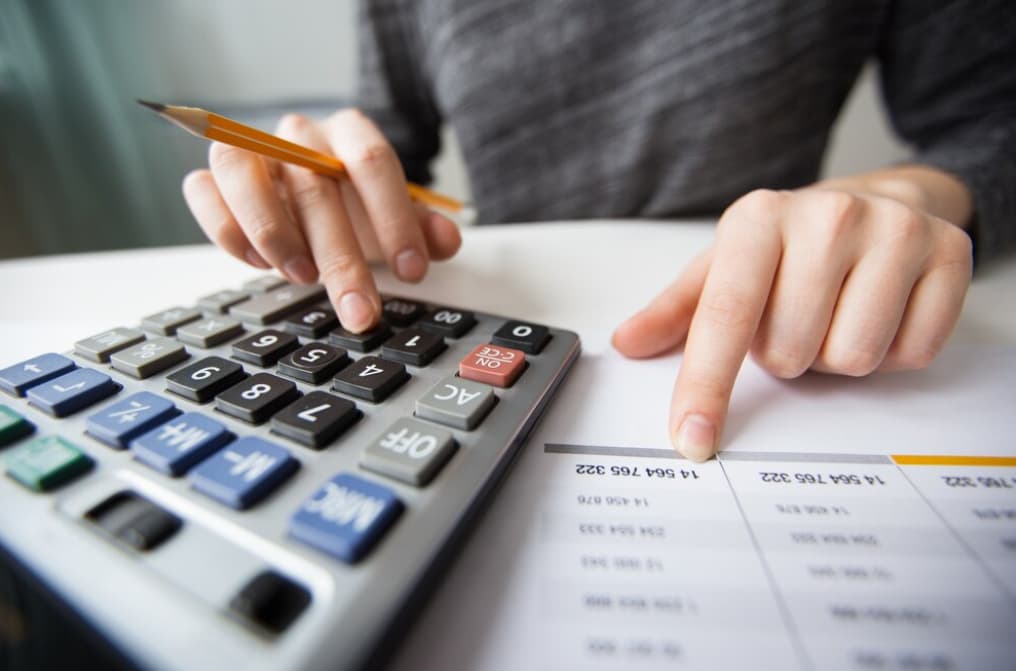 Close-up of a person's hands using a calculator and pointing at a financial document