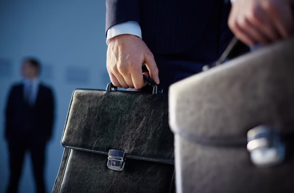 A businessman holding a briefcase with another person in the background