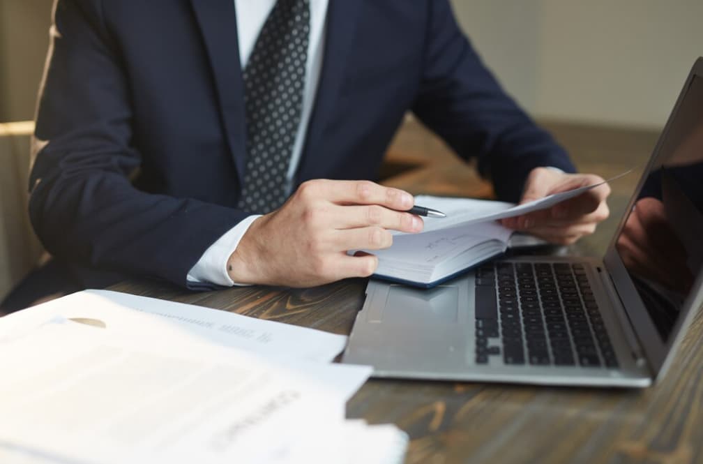 A businessman reviewing documents beside a laptop