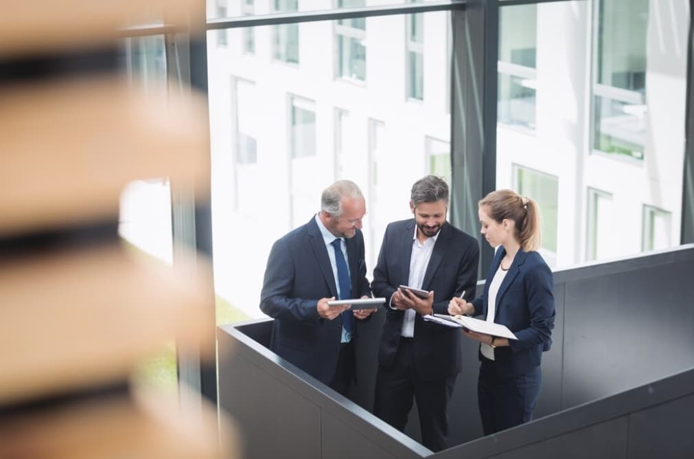 Three professionals discussing with a tablet and documents in an office building