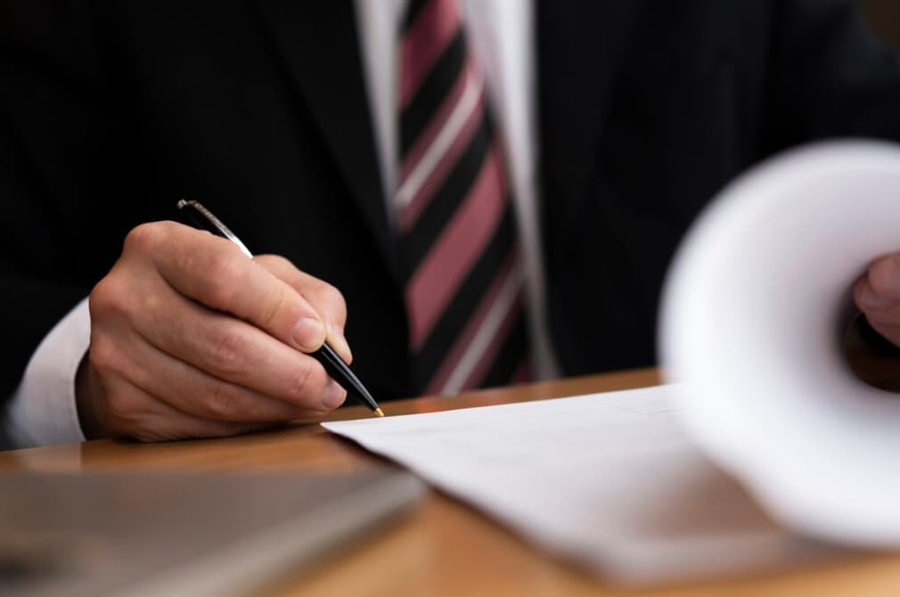 A man in a suit signing a document at a desk