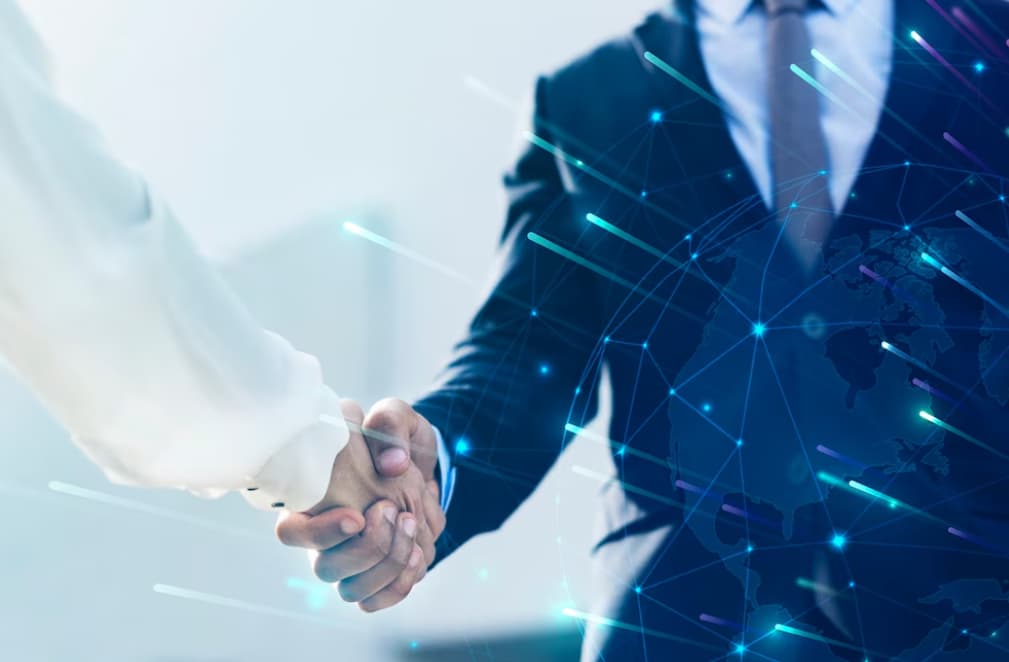 Two professionals shaking hands with a digital world map overlay